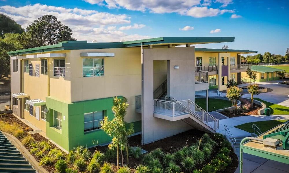 Tan and green building with bushes around the side