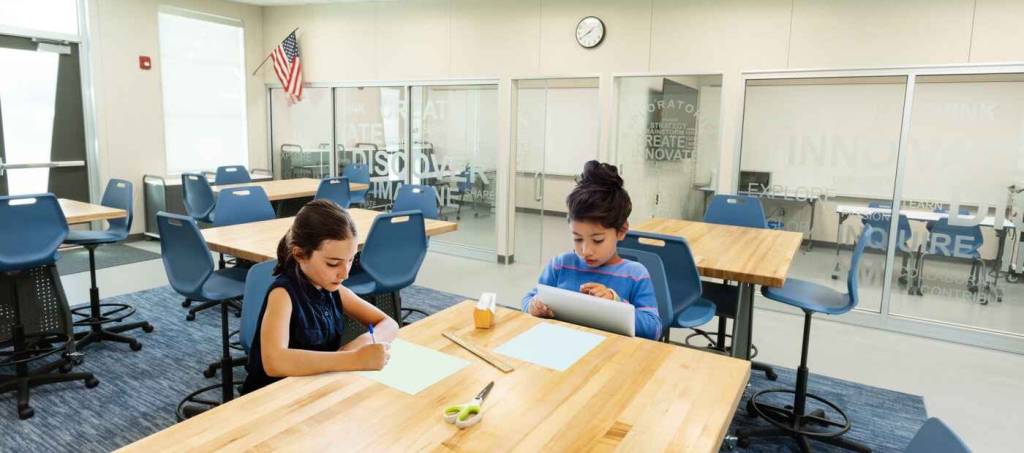 Two students sitting at a table in a classroom, engaged in a discussion and working on their assignments.