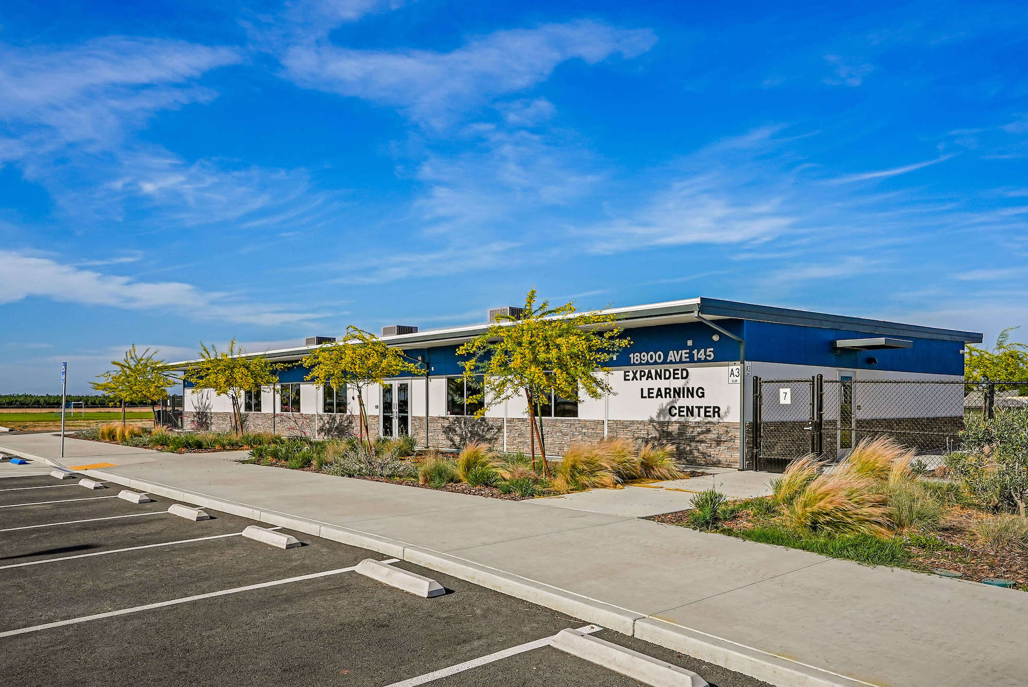 Exterior of a single-story building with the words "Expanded Learning Center" on it, trees and plants along the sidewalk, and a clear blue sky overhead.