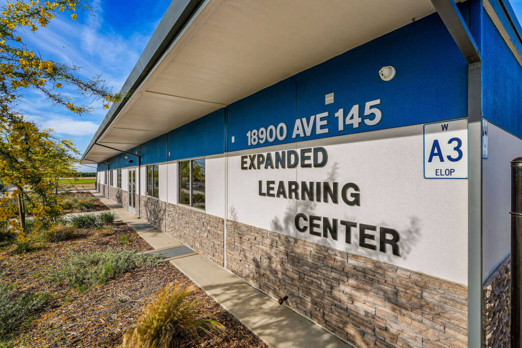 Close-up of an exterior wall with the address "18900 Ave 145" and the words "Expanded Learning Center" in large letters, with windows and landscaping in view.